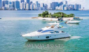 The 60’ Azimut Yacht ‘Wine Down’ cruises near a lively sandbar in Miami, surrounded by crystal-clear water and other anchored boats. The yacht’s sleek white profile and spacious flybridge stand out, while people gather on the island behind it, enjoying water activities and beachside fun. In the distance, the iconic Miami skyline rises, framing this perfect blend of luxury, nature, and city energy.