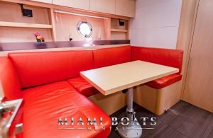 The dining area of the 46' Beneteau yacht. Red couch and wooden table.