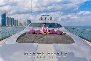 Man sitting on the bow of the 92' Mangusta Luxury Yacht. Miami Downtown on the background.