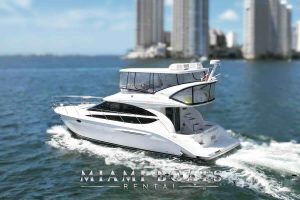 The side view of the 45’ Meridian flybridge yacht in Miami with the Biscayne Bay in the background. At the bottom center is Miami Boats Rental company logo. A flybridge yacht cruising through the waters in Miami. The sleek white yacht features a spacious flybridge enclosed in clear panels, modern curves, and an inviting stairway leading to the swim platform.