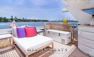 A luxurious entertainment area on the "Casual" Dominator Super Yacht, showcasing the flybridge's full bar, inviting sofas, and stylish wooden floors, adorned with tasteful white and purple pillows.