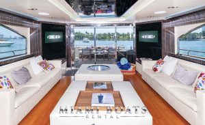 The opulent Dominator Super Yacht "Casual" features a flybridge bar, cozy sofas with white and purple pillows, and polished wooden floors, offering a lavish atmosphere for guests to unwind.