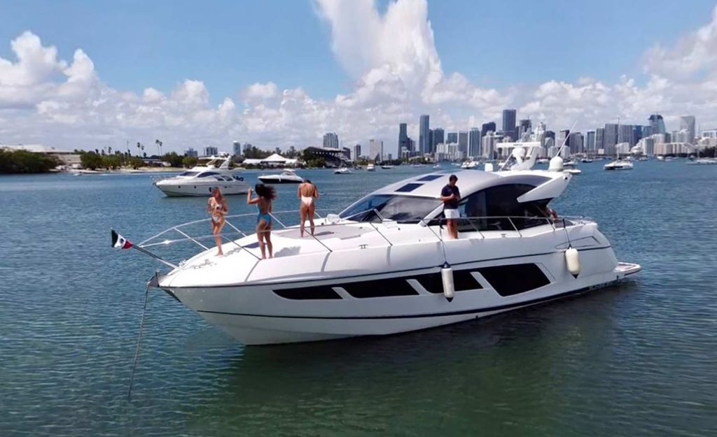 Yacht Rental Miami. Sunseeker Yacht Predator 60ff. The Sport Boat on the water in Miami, and people are having fun in the front of the boat in good weather.