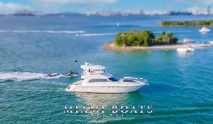 The 55’ Sea Ray Sedan ‘Island Itch’ yacht cruising past a tropical island near Miami, accompanied by jet skis. The yacht’s sleek profile and flybridge shine under the clear skies, capturing the spirit of adventure and luxury.