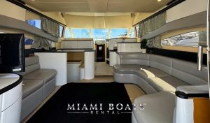 Spacious and modern saloon interior of the 60-foot Viking Yacht named Princess, featuring elegant gray leather seating, a black carpet, white cabinetry, and large windows providing ample natural light. The Miami Boats Rental logo is visible at the bottom of the image.