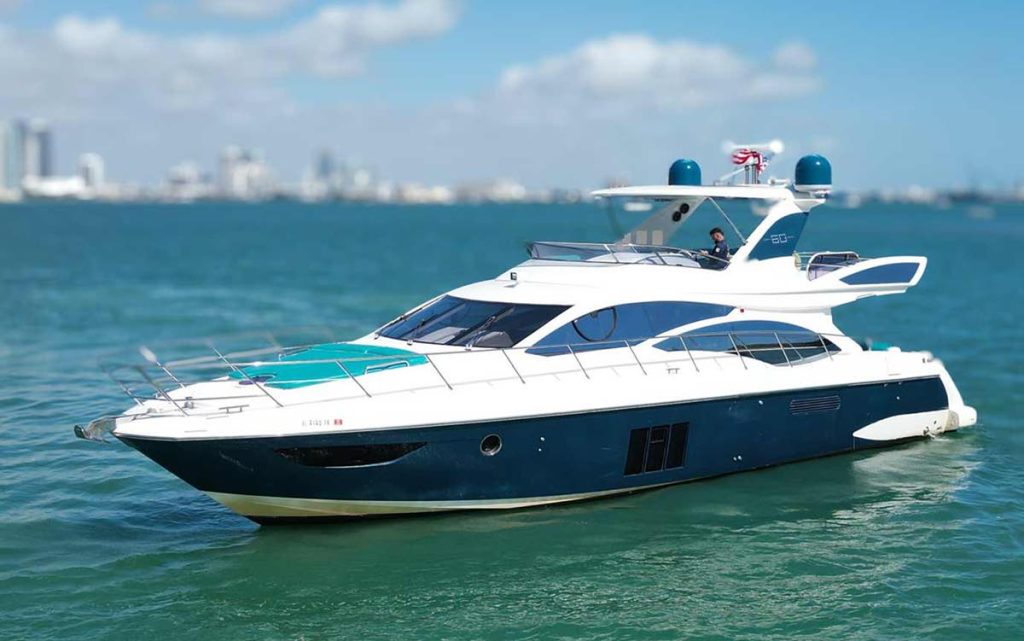 This image showcases the Luxury Yacht Azimut 'TITO' 60 luxury yacht, as it cruises on the serene waters off Miami's coast. The yacht features a striking dark blue hull with a white superstructure and teal accents that complement the vibrant Miami backdrop. The sleek, modern design of the yacht is highlighted by its streamlined windows and multiple decks, offering spacious areas for relaxation and viewing. The upper deck includes a helm station and additional seating, enhancing the outdoor boating experience. The photograph captures the essence of luxury yachting with Miami's skyline in the background, emphasizing a perfect blend of high-end leisure and the city’s dynamic atmosphere.