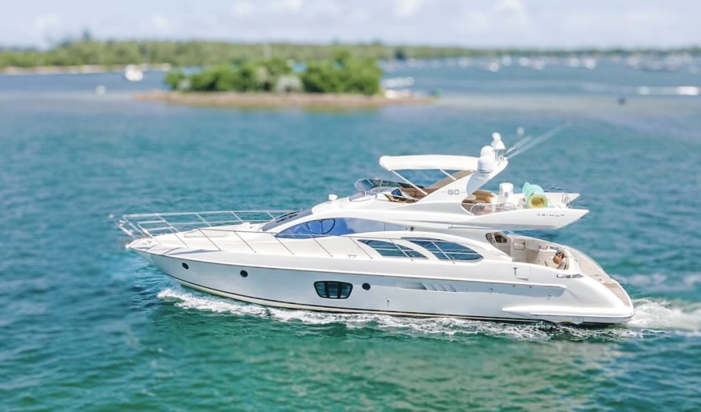 Luxury Azimut Yacht Wine Down with a panoramic view, sailing on the blue water in Miami Beach. The Azimut Yacht features a spacious flybridge area, perfect for the ultimate Miami boat party. The picnic islands in the background are located in Miami Beach.
