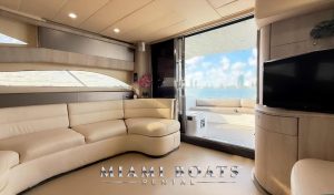 Luxury interior of a 60’ Viking yacht available for rent in Miami, featuring a spacious salon with plush cream-colored leather seating, a flat-screen TV, and modern wood paneling. Sliding glass doors open to an outdoor deck with additional seating and stunning ocean views of the Miami skyline. “Miami Boats Rental” branding is displayed at the bottom. Perfect for private yacht charters and luxury boat experiences.