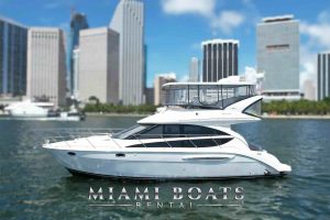 Side view of the 45’ Meridian yacht from Miami Boats Rental cruising calmly through Biscayne Bay. The yacht features sleek, modern lines, a fully enclosed flybridge, and panoramic windows offering stunning waterfront views. The backdrop showcases downtown Miami’s iconic skyline, highlighting the perfect blend of luxury boating and city sophistication.