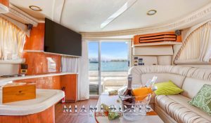 Luxurious lounge area on the Sea Ray 55’ “Island Itch” with a curved leather sofa, flat-screen TV, and sliding glass doors that open to a rear deck overlooking the water. A champagne bucket and vibrant green accent pillows add a touch of elegance.