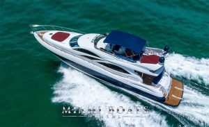 Aerial view of the SlipTease Sunseeker Manhattan Yacht with Miami Boats Rental logo cruising in Miami, with a clear view of the yacht's sun deck and the canopy. The overhead shot captures the vessel cutting through the ocean, leaving a frothy white wake behind, symbolizing luxury and adventure.