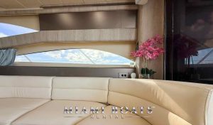 Luxury yacht interior with ocean views – A close-up of the plush cream-colored leather seating inside a 60’ Viking yacht, accented with elegant wood paneling and a decorative pink orchid. Large windows provide stunning ocean views. Perfect for luxury yacht rentals and private charters in Miami. “Miami Boats Rental” branding is displayed at the bottom.