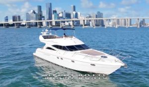 Luxury yacht rental in Miami – a sleek 60’ Viking Princess yacht cruising on the blue waters with the stunning Miami Downtown skyline and bridge in the background. Featuring a spacious sunbathing area on the bow, a stylish flybridge with a shaded seating area, and modern amenities, this yacht is perfect for private charters, special events, and luxury boat experiences. “Miami Boats Rental” branding is displayed at the bottom.