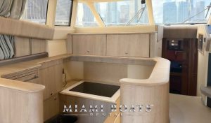 Luxury yacht rental in Miami – the modern kitchen of a 60’ Viking yacht featuring elegant wood cabinetry, a built-in stovetop, and ample counter space. Large windows offer stunning views of the Miami skyline, while a doorway leads to the yacht’s cozy cabin. Perfect for private charters, luxury boat rentals, and exclusive yacht experiences. “Miami Boats Rental” branding is displayed at the bottom.